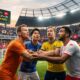 Sebuah close-up dramatis dari empat pemain sepak bola yang mengenakan jersey Belanda, Jepang, Swedia, dan Tunisia sedang saling berpelukan dan berhadapan di lapangan yang disinari lampu sorot. Ekspresi wajah mereka penuh determinasi dan ketegangan. Di latar belakang, penonton di stadion meriah dengan spanduk-spanduk tim. Sebuah layar besar di atas tribun bertuliskan 'KLASMEN PANAS! Belanda vs Tunisia, Jepang vs Swedia, Semua Tim Berpeluang Lolos!'