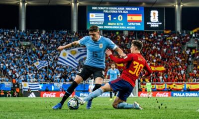 Foto aksi pertandingan Piala Dunia 2026 antara Uruguay dan Spanyol di Stadion Guadalajara, Meksiko. Gelandang Uruguay Federico Valverde (nomor 15) sedang mendribel bola sambil dibayang-bayangi oleh pemain Spanyol Gavi (nomor 30) yang mencoba melakukan tekel sliding. Di latar belakang, papan skor menunjukkan skor 1-1 pada menit ke-78.
